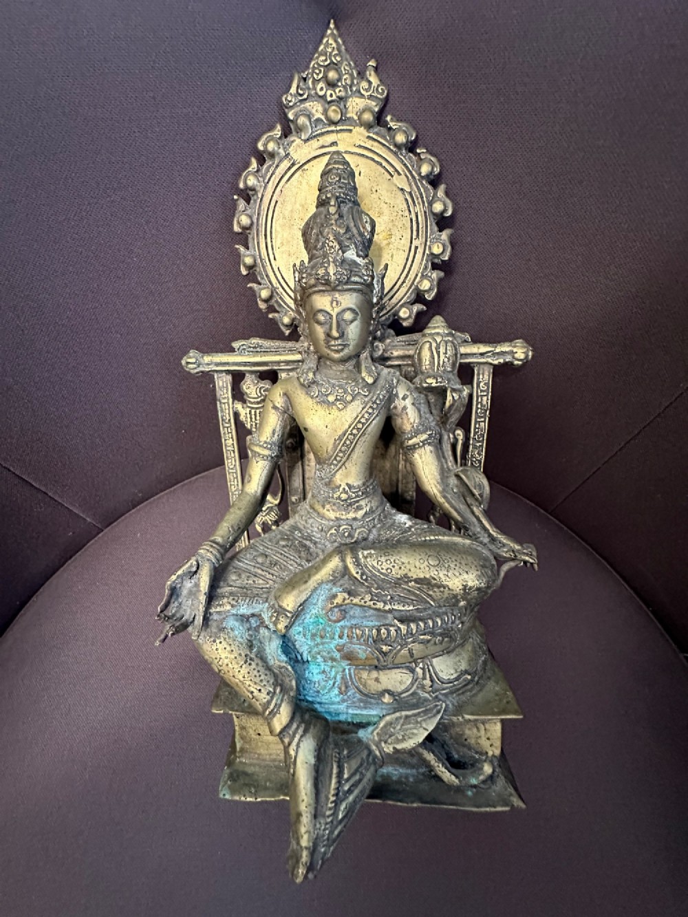 An antique cast bronze figure of Green Tara seated on an elaborate throne with a flaming halo backpiece and visible green patination. View XIII