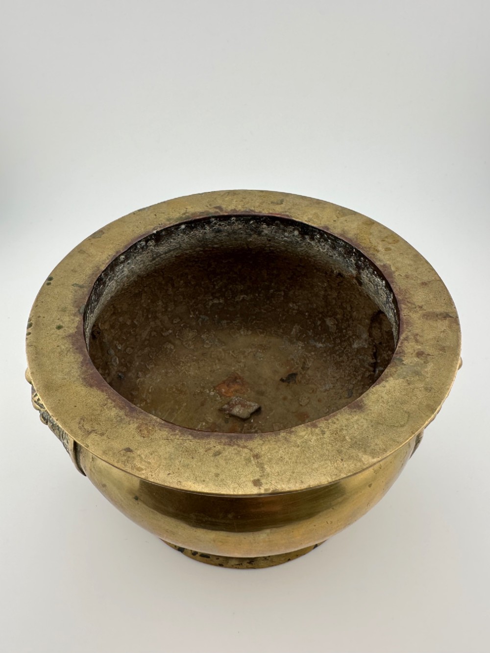 A rounded antique brass Chinese censer featuring a flared rim, pedestal base, and sculpted lion mask handles on either side. View VI