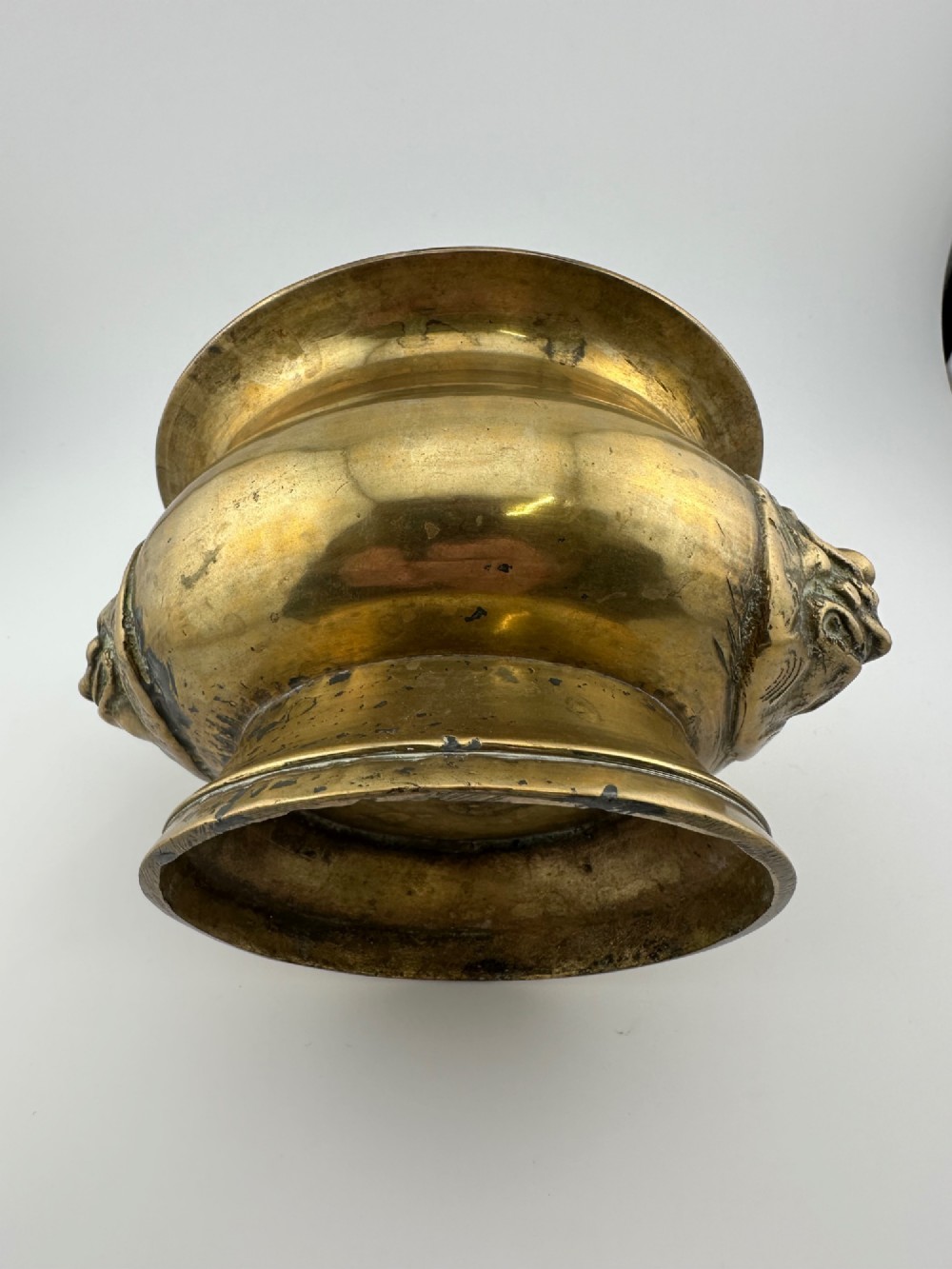 A rounded antique brass Chinese censer featuring a flared rim, pedestal base, and sculpted lion mask handles on either side. View VII