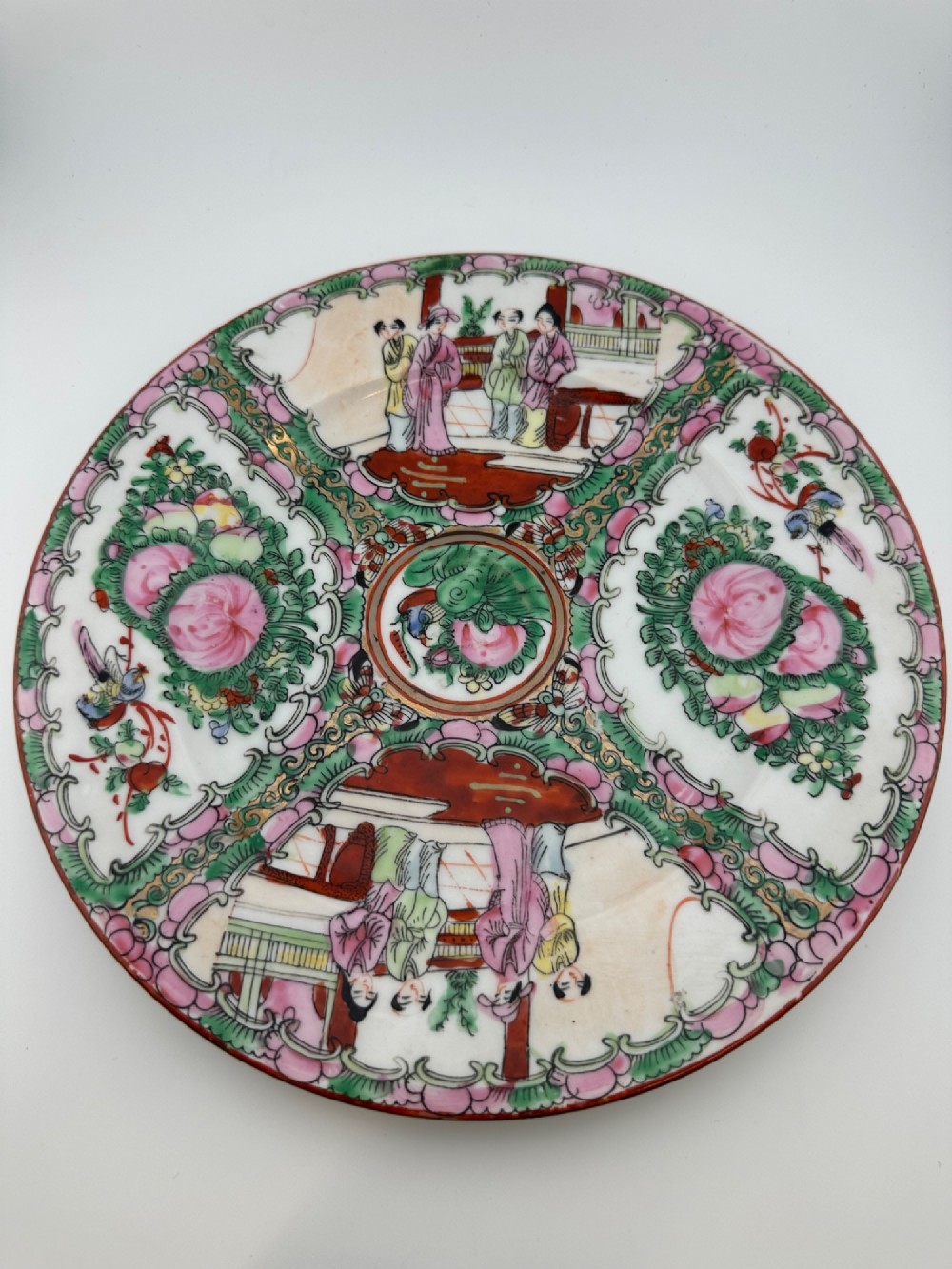 A circular hand-painted ceramic charger with alternating panels depicting human figures and floral motifs in green, pink, and red enamels with gold accents.