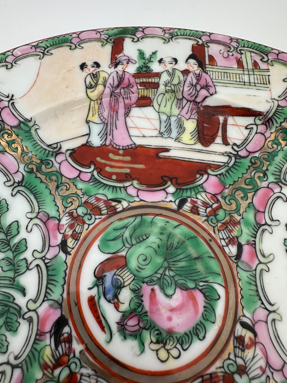 A circular hand-painted ceramic charger with alternating panels depicting human figures and floral motifs in green, pink, and red enamels with gold accents. View II