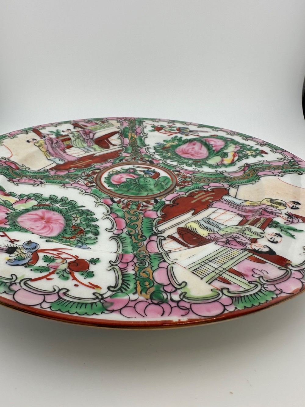 A circular hand-painted ceramic charger with alternating panels depicting human figures and floral motifs in green, pink, and red enamels with gold accents. View VI