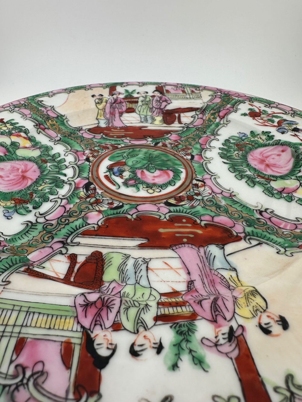 A circular hand-painted ceramic charger with alternating panels depicting human figures and floral motifs in green, pink, and red enamels with gold accents. View VII