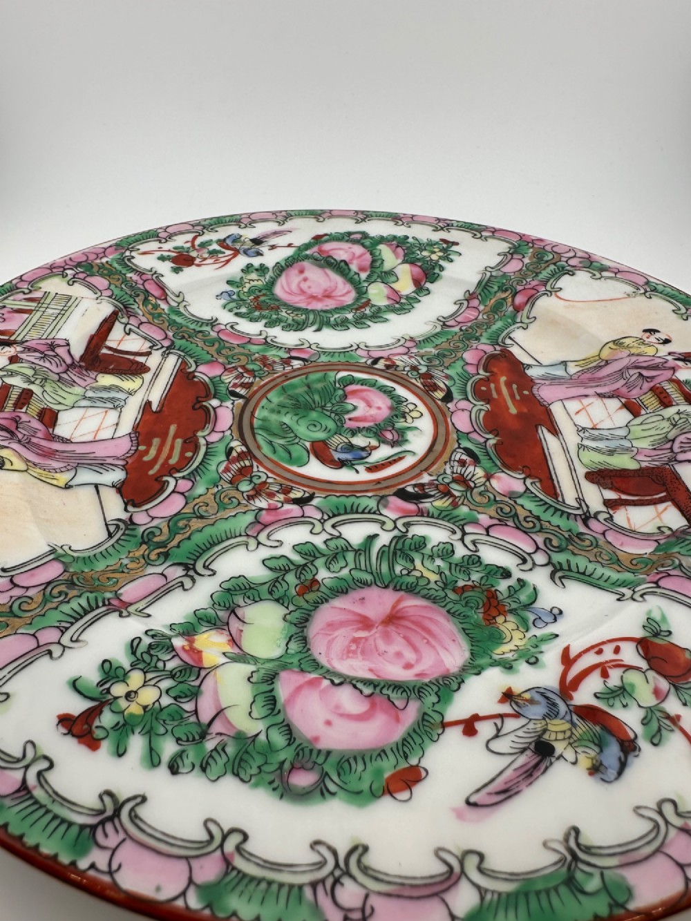 A circular hand-painted ceramic charger with alternating panels depicting human figures and floral motifs in green, pink, and red enamels with gold accents. View VIII
