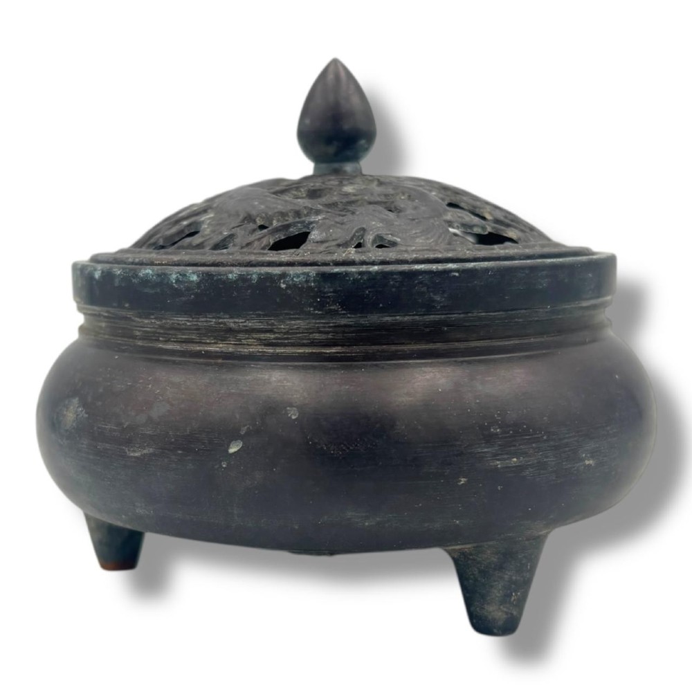 A dark patinated bronze tripod censer featuring a rounded body, three short tapered feet, and a pierced openwork lid topped with a bud finial.