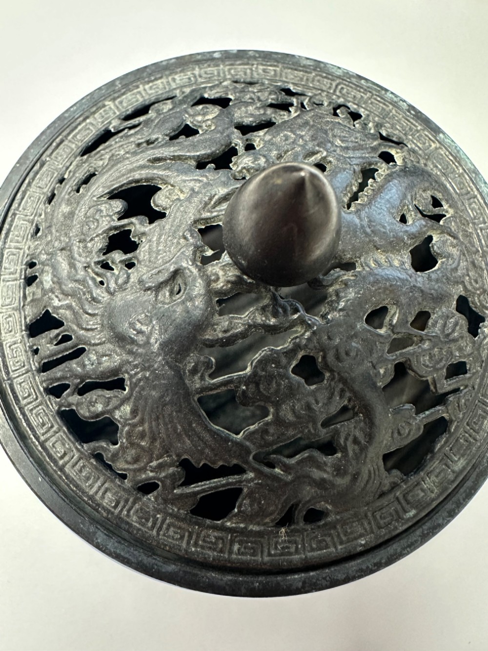 A dark patinated bronze tripod censer featuring a rounded body, three short tapered feet, and a pierced openwork lid topped with a bud finial. View X