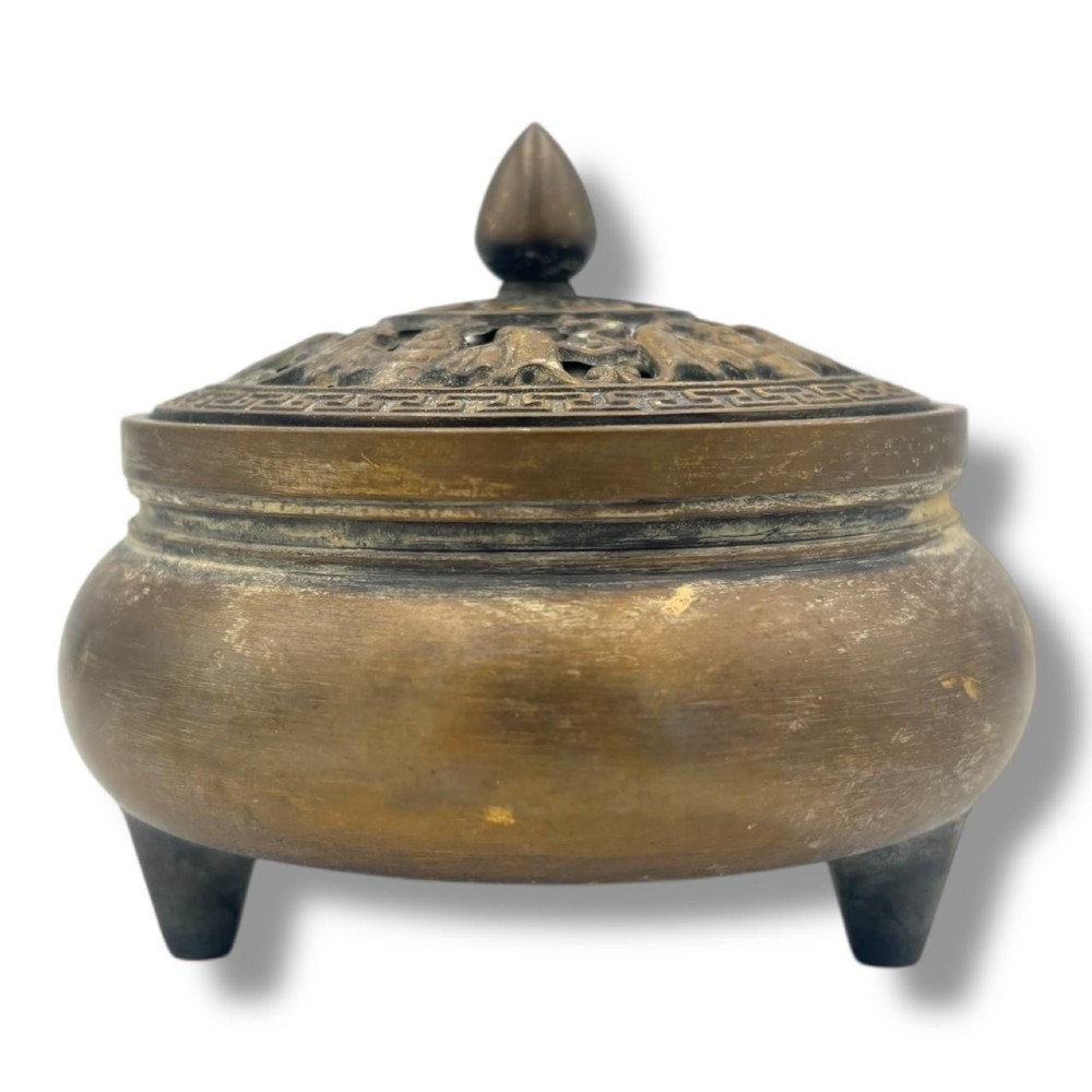 A Chinese bronze tripod censer featuring a compressed circular body, three tapered feet, and a reticulated lotus lid topped with a pointed finial.