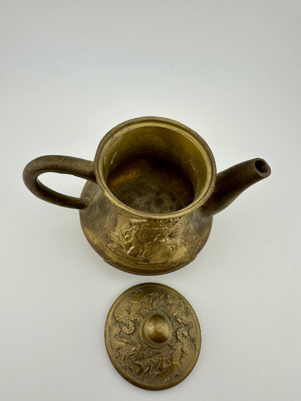A cast brass Chinese teapot featuring raised relief figures, traditional Chinese characters along the base, a curved spout, handle, and a round lid knob. View V