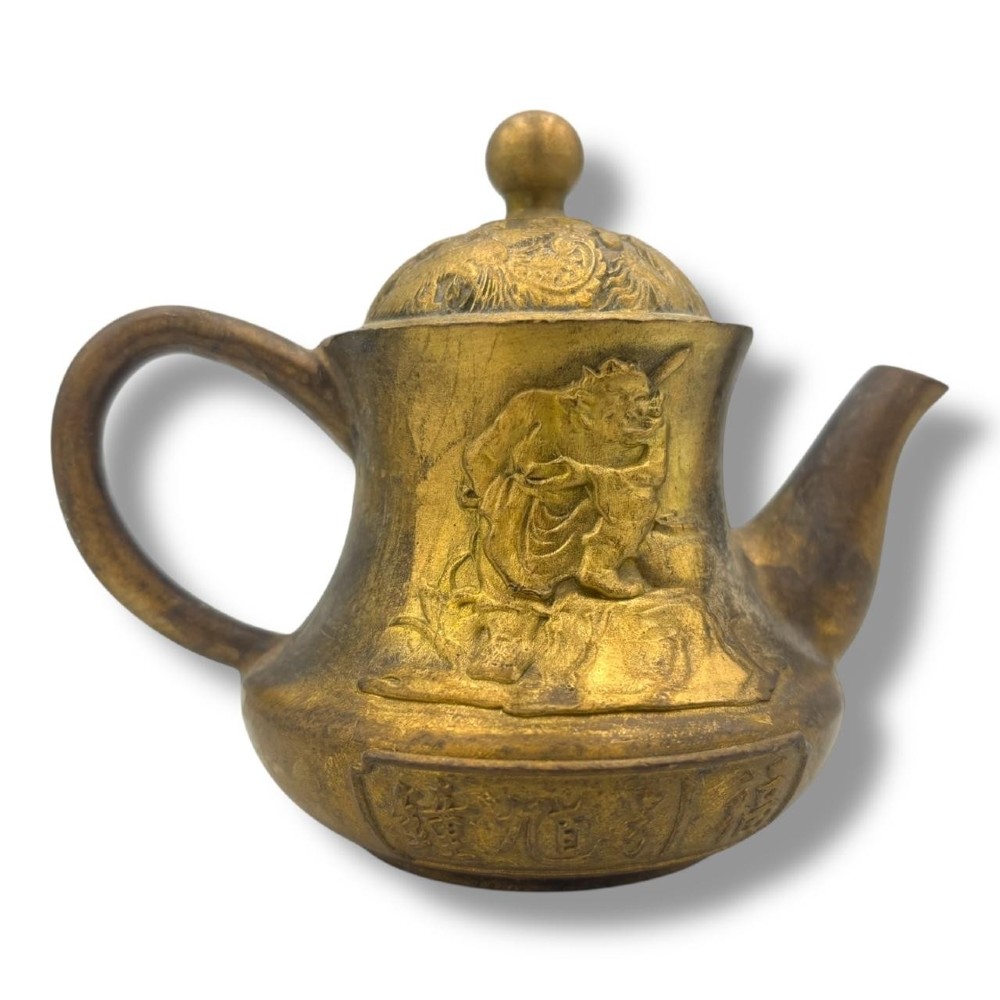 A cast brass Chinese teapot featuring raised relief figures, traditional Chinese characters along the base, a curved spout, handle, and a round lid knob. View IX