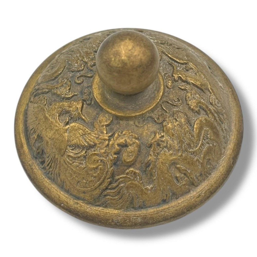 A cast brass Chinese teapot featuring raised relief figures, traditional Chinese characters along the base, a curved spout, handle, and a round lid knob. View X