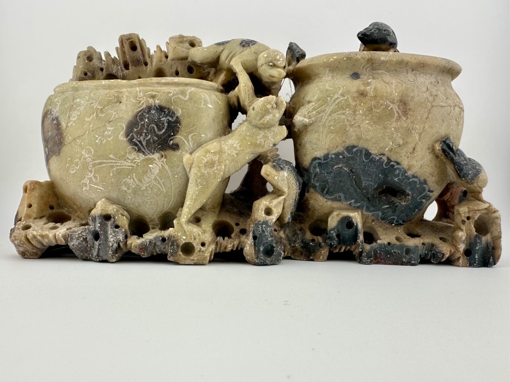 An antique Chinese carved soapstone double brush washer featuring two vessel shapes supported by carved animals and pierced rockwork in shades of mottled green, cream, and dark grey.