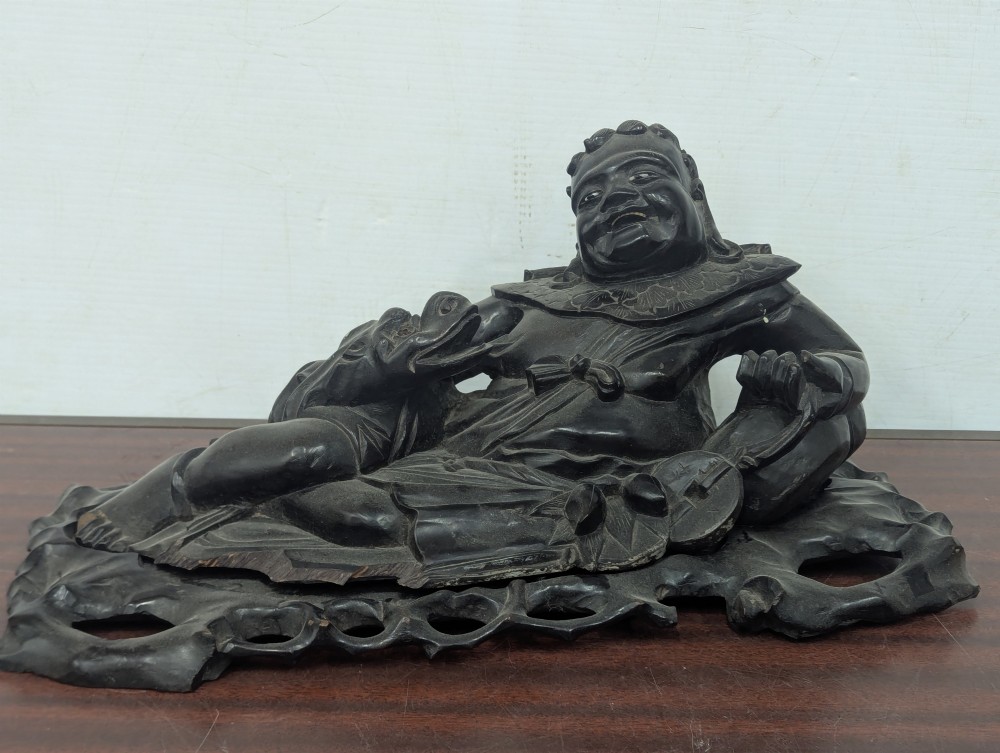 A late Qing Dynasty dark carved hardwood figure depicting a reclining Budai resting on an openwork carved wooden base. View II