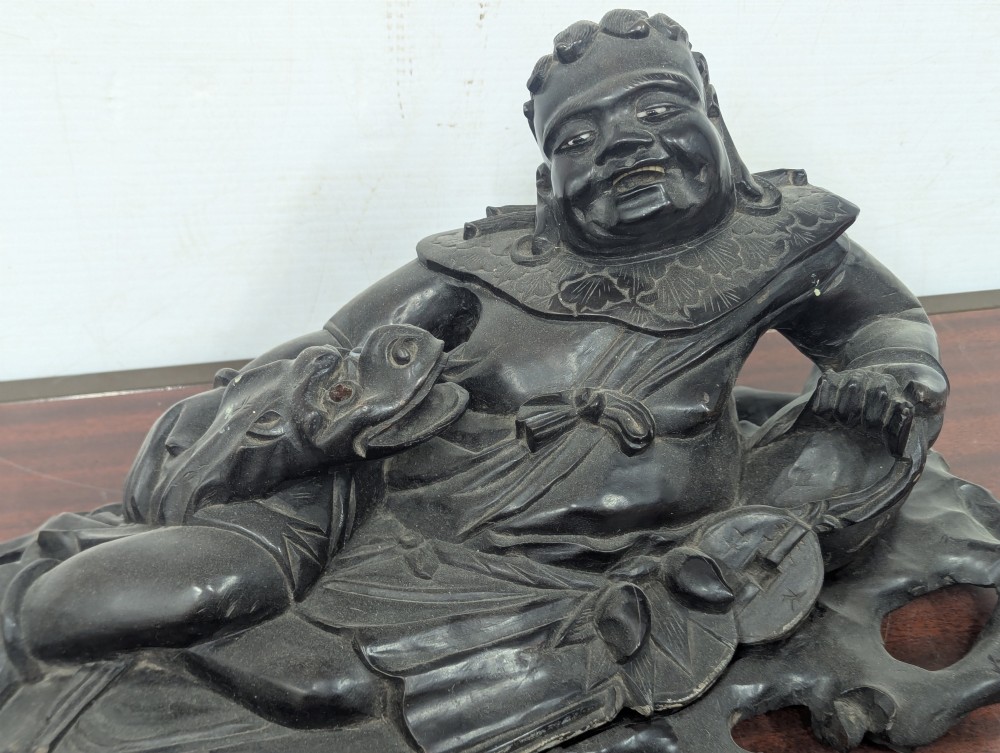 A late Qing Dynasty dark carved hardwood figure depicting a reclining Budai resting on an openwork carved wooden base. View V
