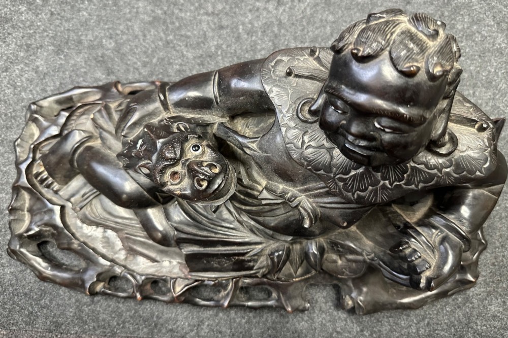 A late Qing Dynasty dark carved hardwood figure depicting a reclining Budai resting on an openwork carved wooden base. View XII