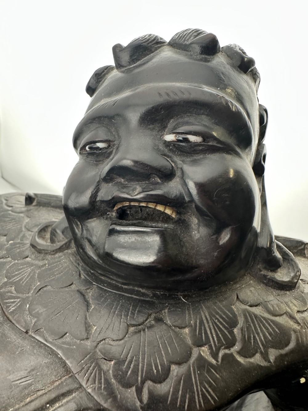 A late Qing Dynasty dark carved hardwood figure depicting a reclining Budai resting on an openwork carved wooden base. View XIII