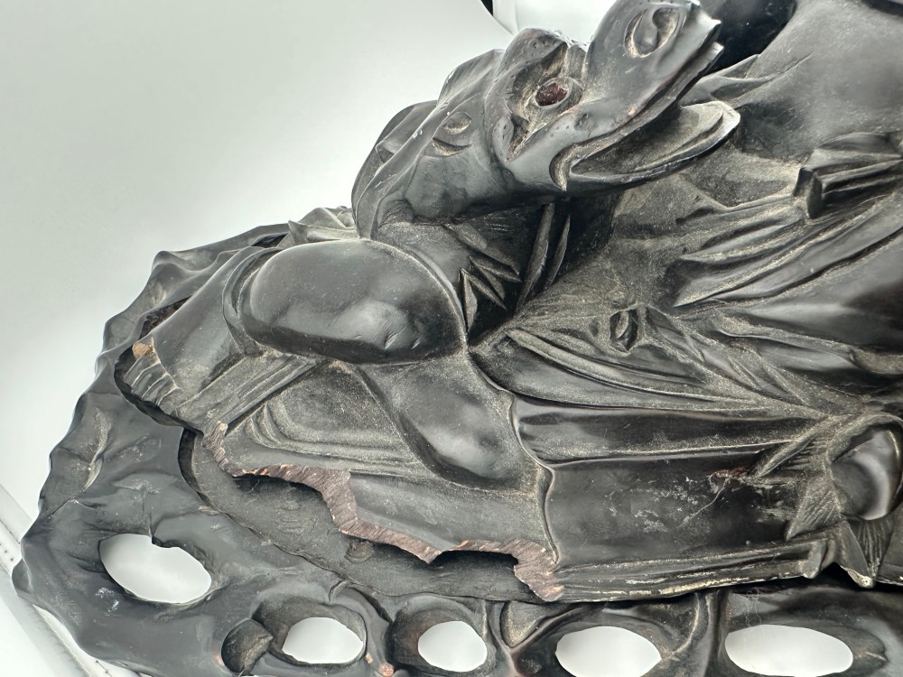 A late Qing Dynasty dark carved hardwood figure depicting a reclining Budai resting on an openwork carved wooden base. View XIV