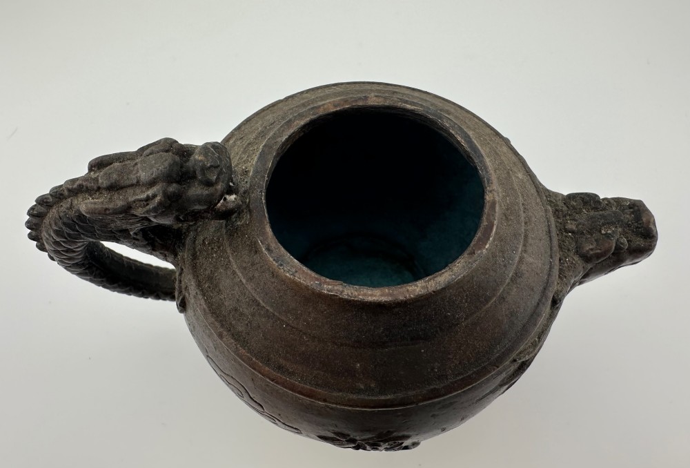 A dark cast bronze Chinese teapot featuring a sculpted dragon handle, a dragon-head spout, and raised Chinese character carvings on the main body. View VI