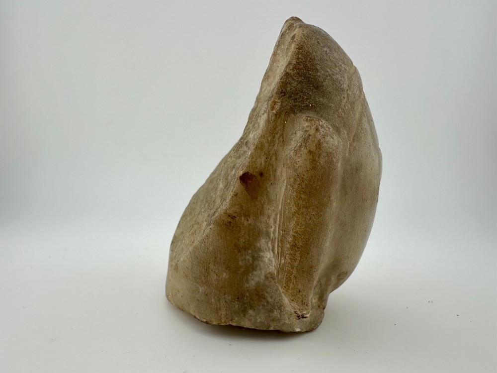 A carved off-white hardstone head fragment featuring facial features, elongated earlobes, and faint traces of gilding across the surface. View IV