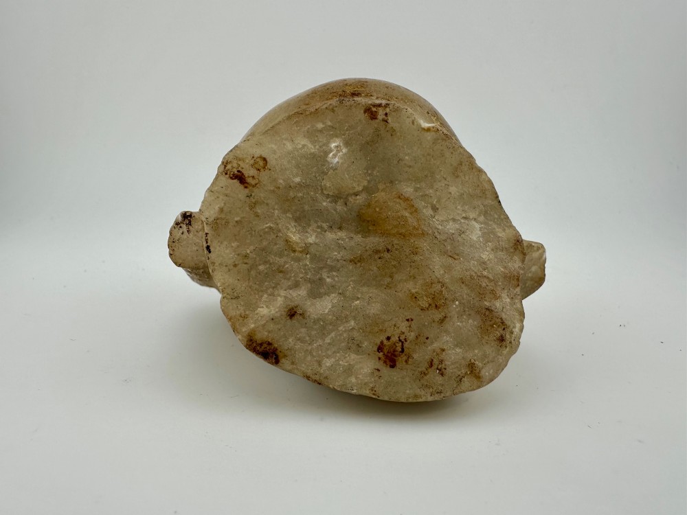 A carved off-white hardstone head fragment featuring facial features, elongated earlobes, and faint traces of gilding across the surface. View V