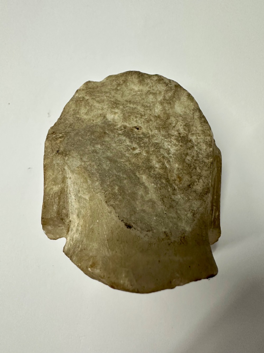 A carved off-white hardstone head fragment featuring facial features, elongated earlobes, and faint traces of gilding across the surface. View IX