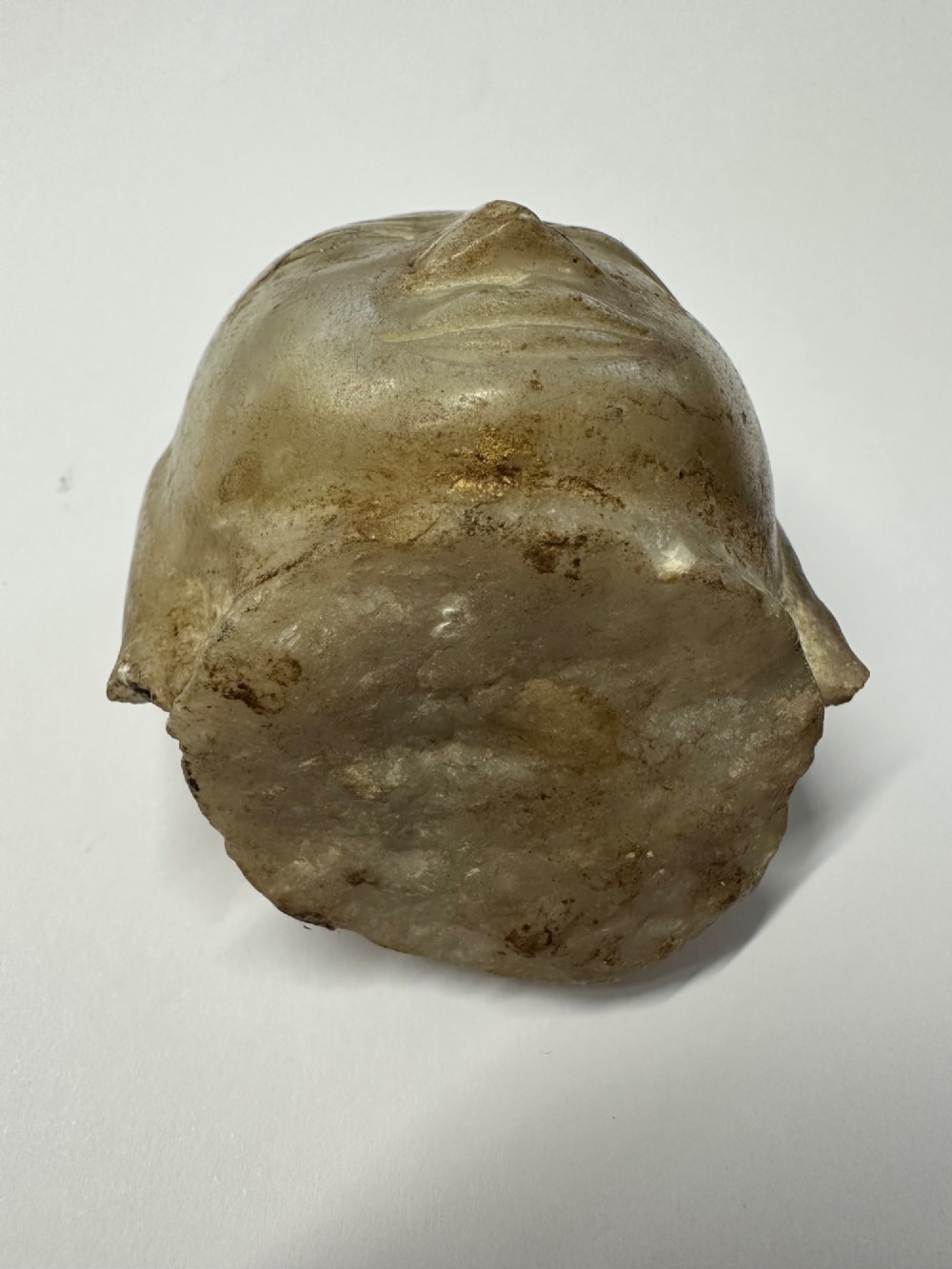 A carved off-white hardstone head fragment featuring facial features, elongated earlobes, and faint traces of gilding across the surface. View XI