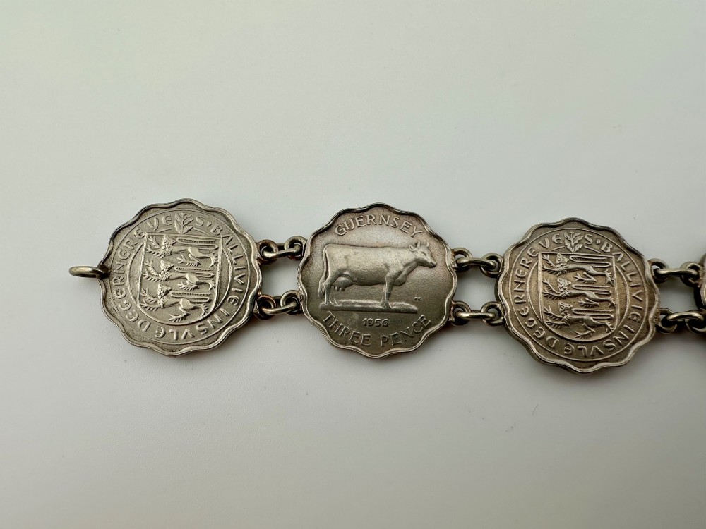 A silver-toned metal bracelet made from scalloped 1956 Guernsey threepence coins featuring a cow and coat of arms, connected to a horseshoe charm and bolt ring clasp. View III