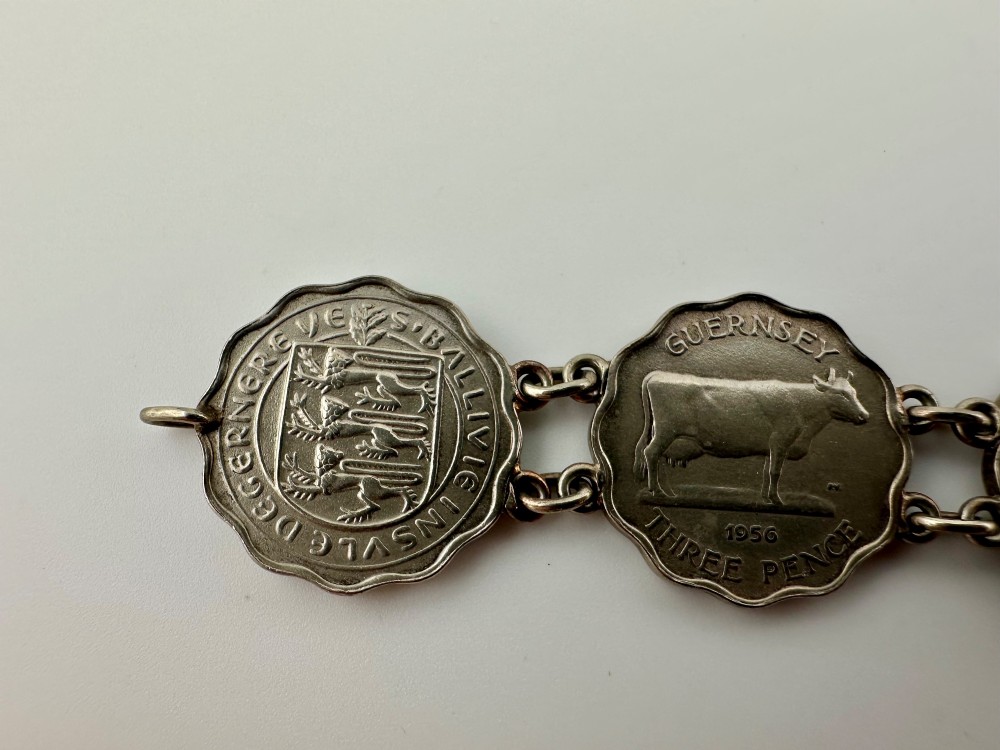 A silver-toned metal bracelet made from scalloped 1956 Guernsey threepence coins featuring a cow and coat of arms, connected to a horseshoe charm and bolt ring clasp. View V