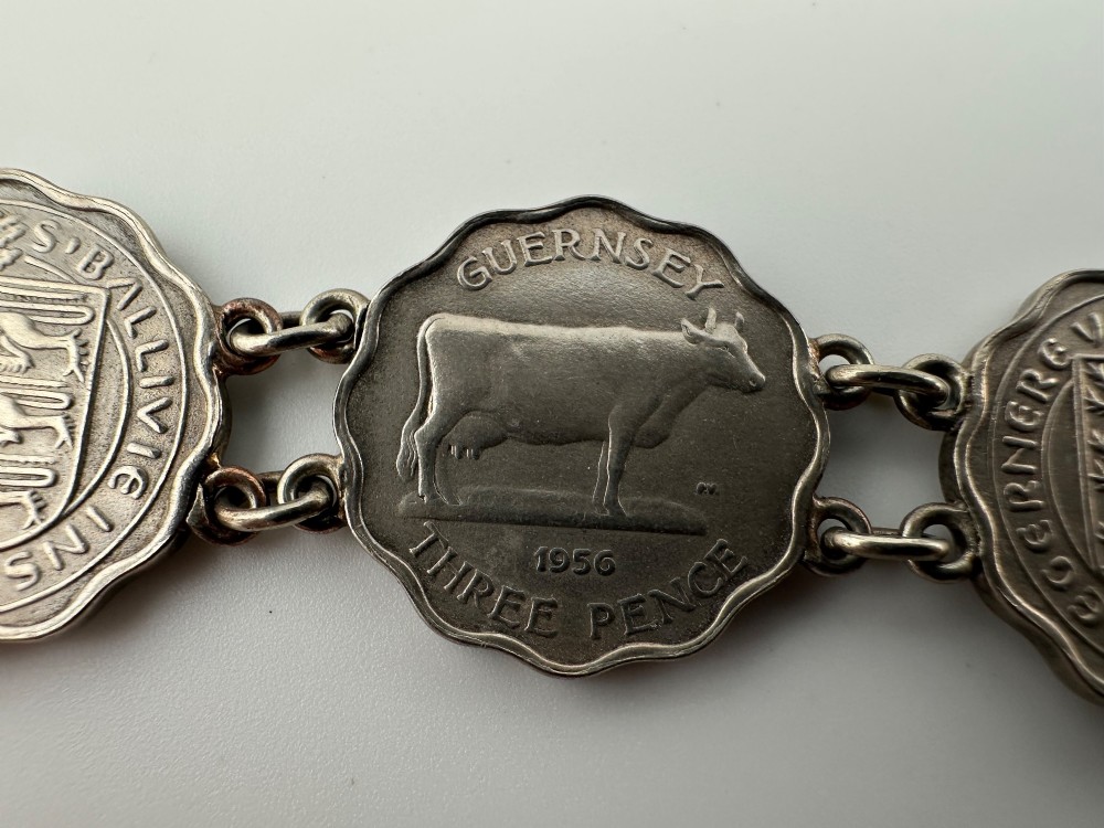 A silver-toned metal bracelet made from scalloped 1956 Guernsey threepence coins featuring a cow and coat of arms, connected to a horseshoe charm and bolt ring clasp. View VII