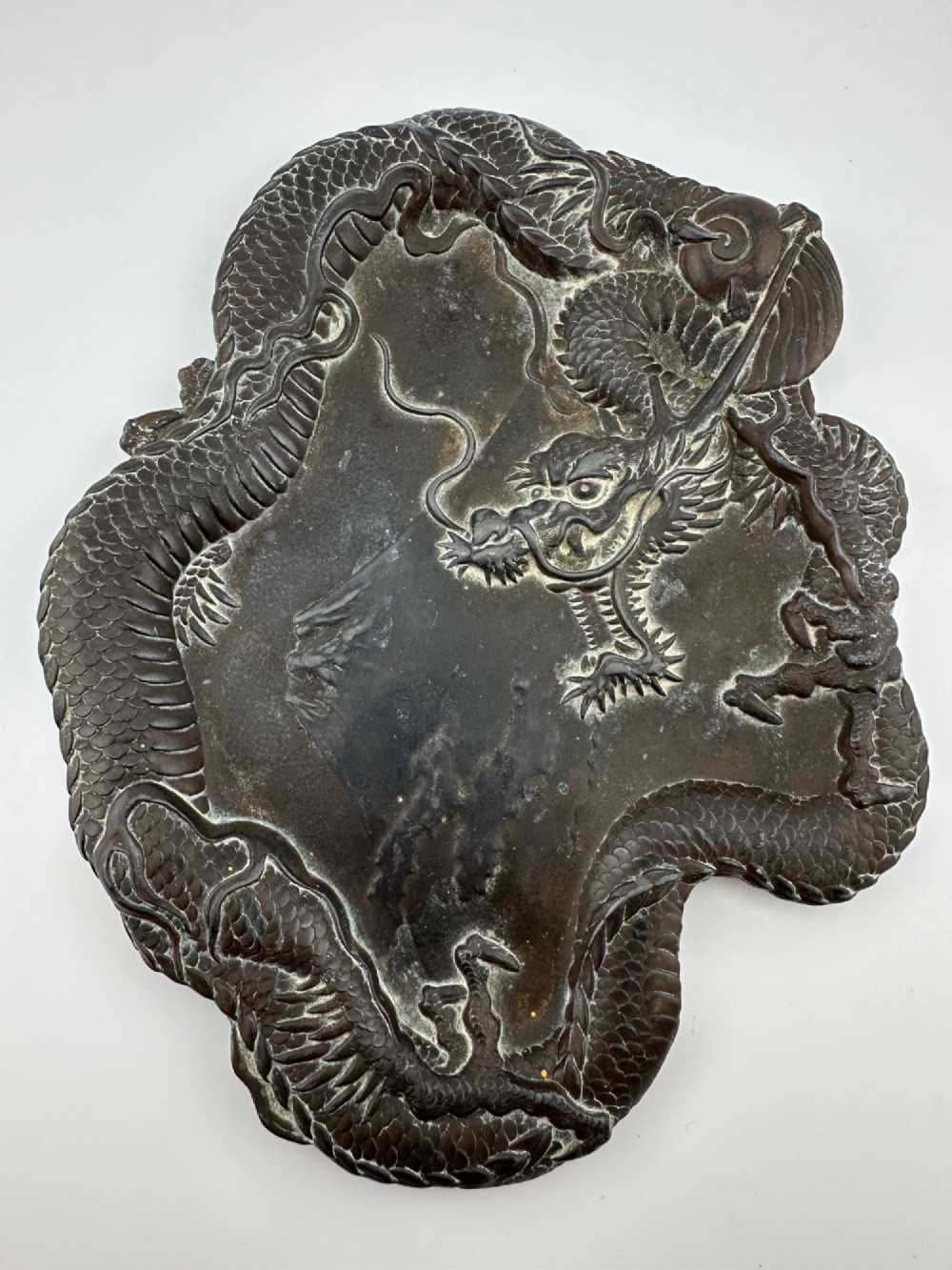 A dark patinated metal tray featuring a raised relief carving of a Japanese dragon coiling around its organic rim.
