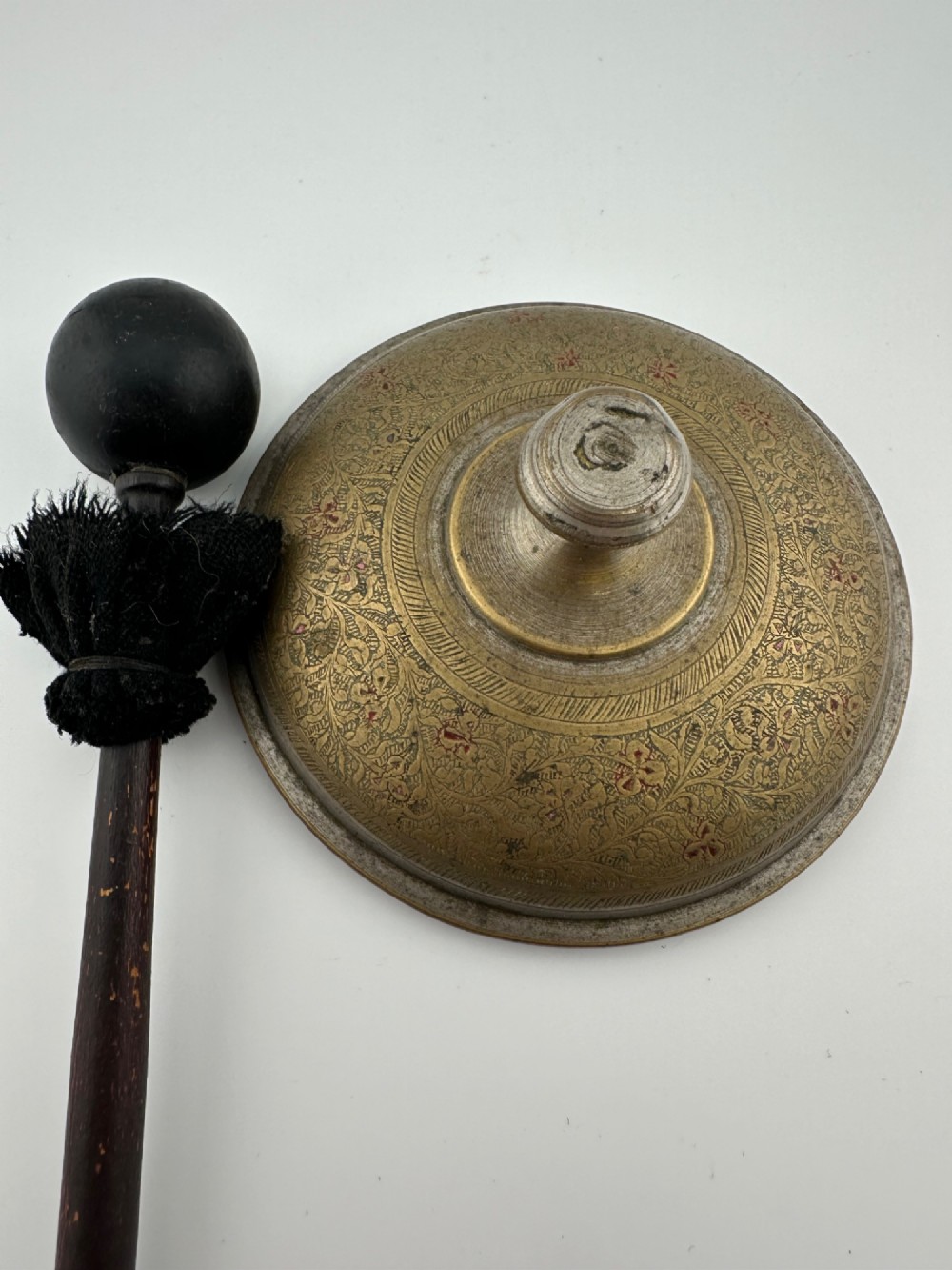 An antique domed Indian brass hand gong with detailed floral engravings, a turned central finial handle, and a dark wooden striker. View V