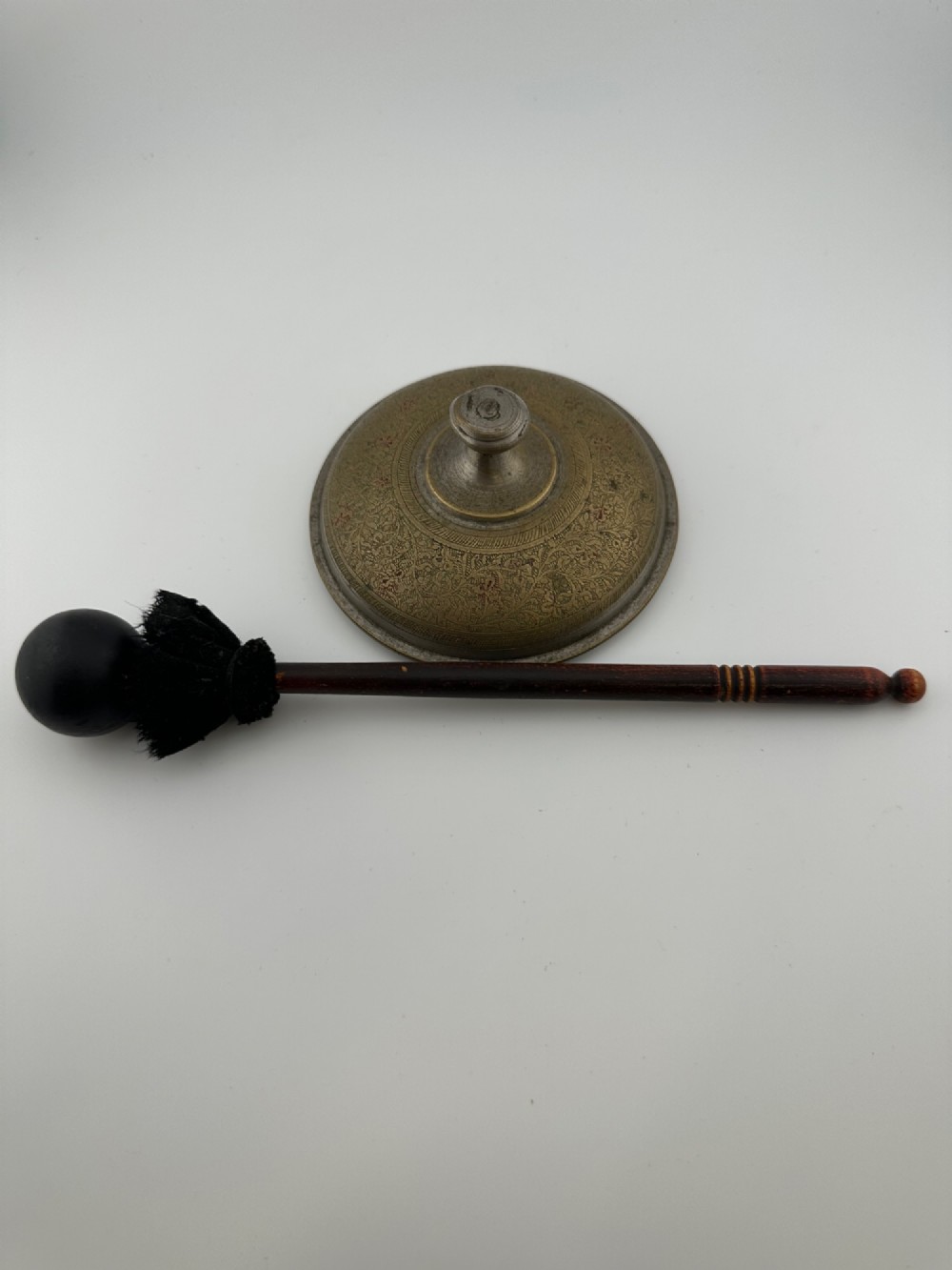 An antique domed Indian brass hand gong with detailed floral engravings, a turned central finial handle, and a dark wooden striker. View X