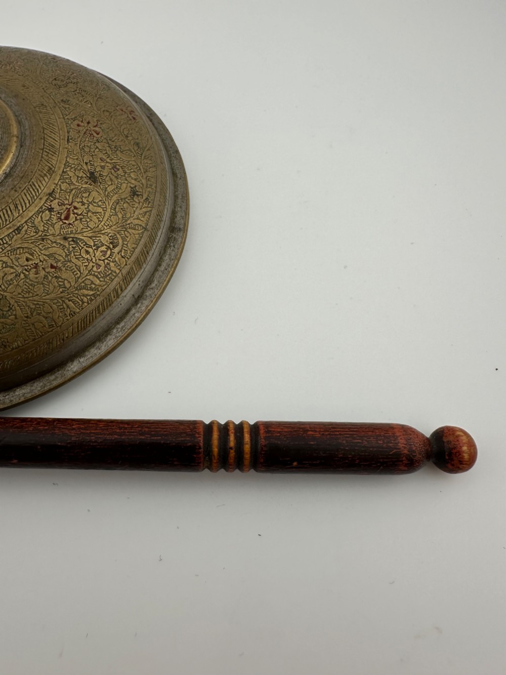 An antique domed Indian brass hand gong with detailed floral engravings, a turned central finial handle, and a dark wooden striker. View XI