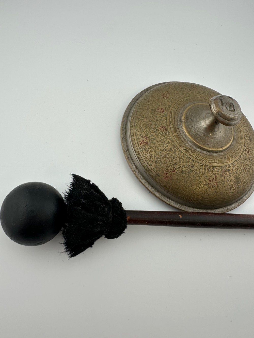 An antique domed Indian brass hand gong with detailed floral engravings, a turned central finial handle, and a dark wooden striker. View XII