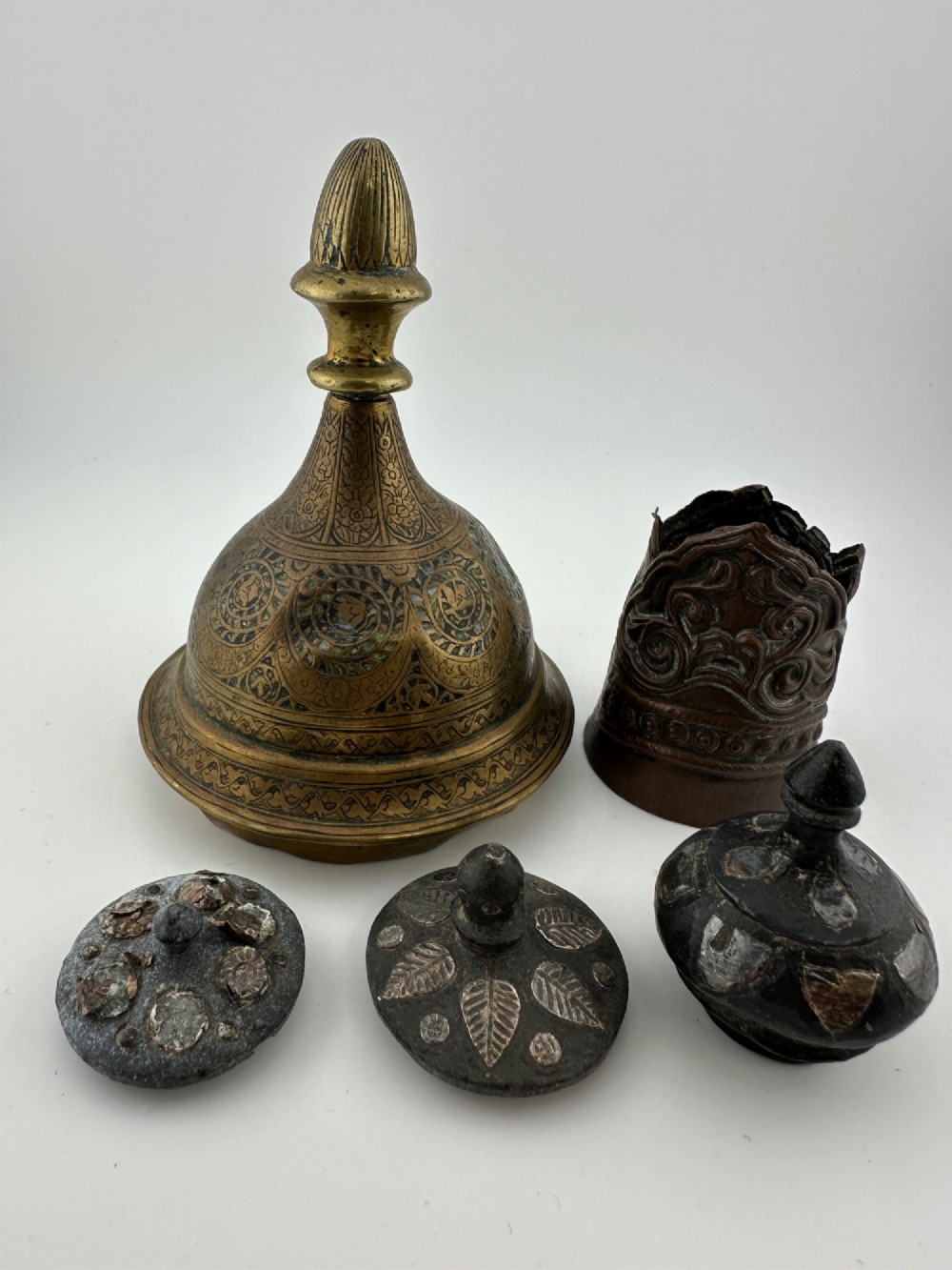 A five-piece group of antique Persian Qajar metalware, including an engraved brass incense burner lid with a finial, a dark carved vessel collar, and three small circular lids. View II