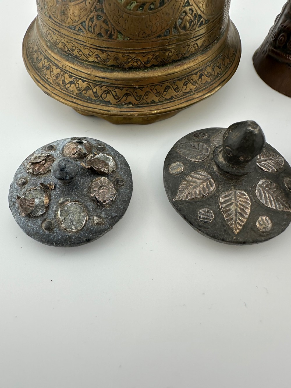 A five-piece group of antique Persian Qajar metalware, including an engraved brass incense burner lid with a finial, a dark carved vessel collar, and three small circular lids. View V