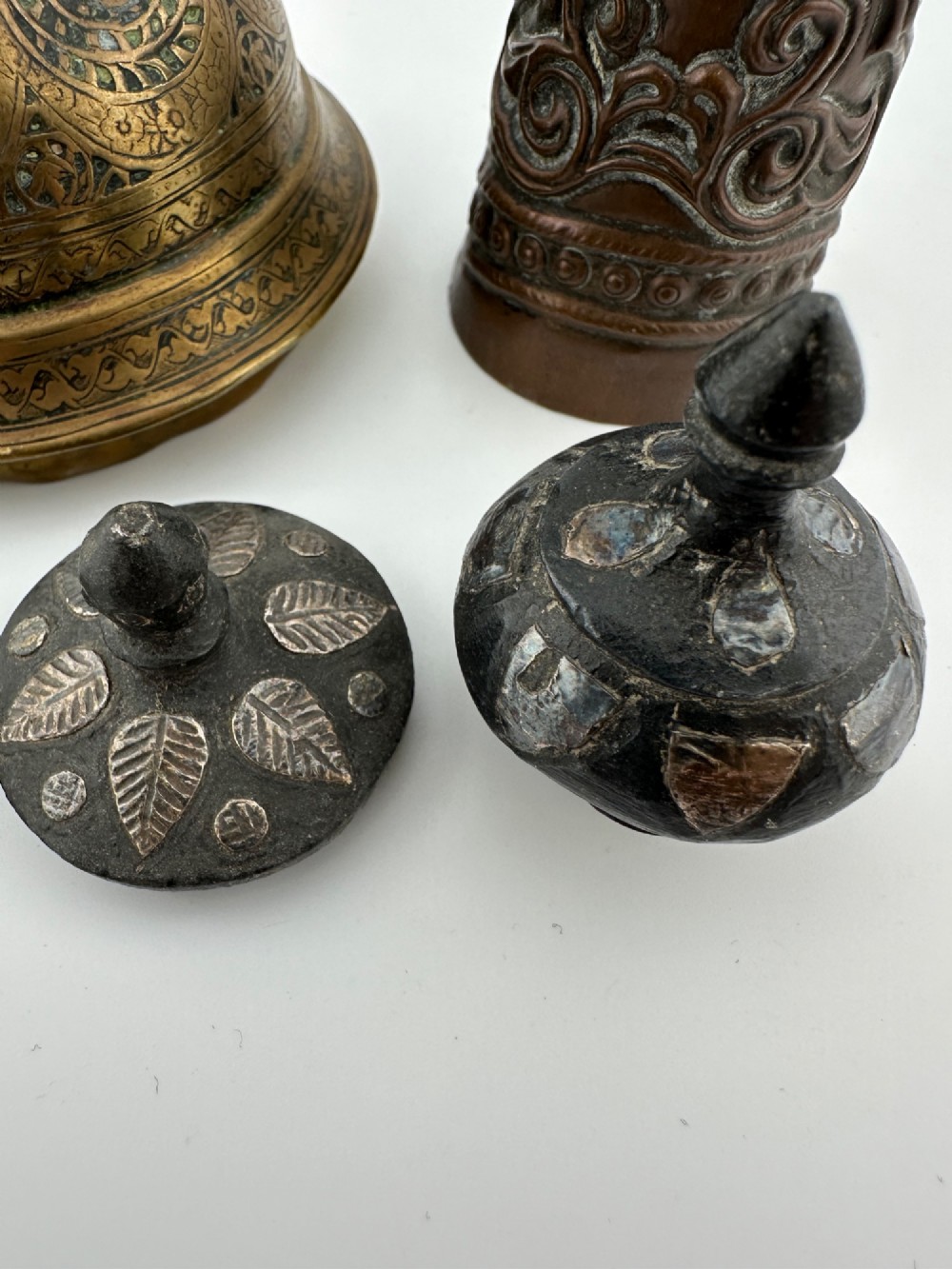A five-piece group of antique Persian Qajar metalware, including an engraved brass incense burner lid with a finial, a dark carved vessel collar, and three small circular lids. View VI