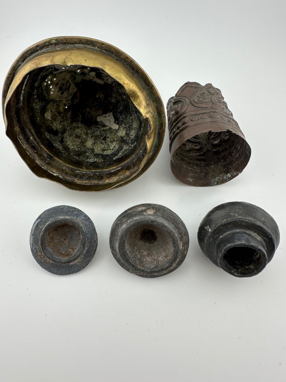 A five-piece group of antique Persian Qajar metalware, including an engraved brass incense burner lid with a finial, a dark carved vessel collar, and three small circular lids. View VII