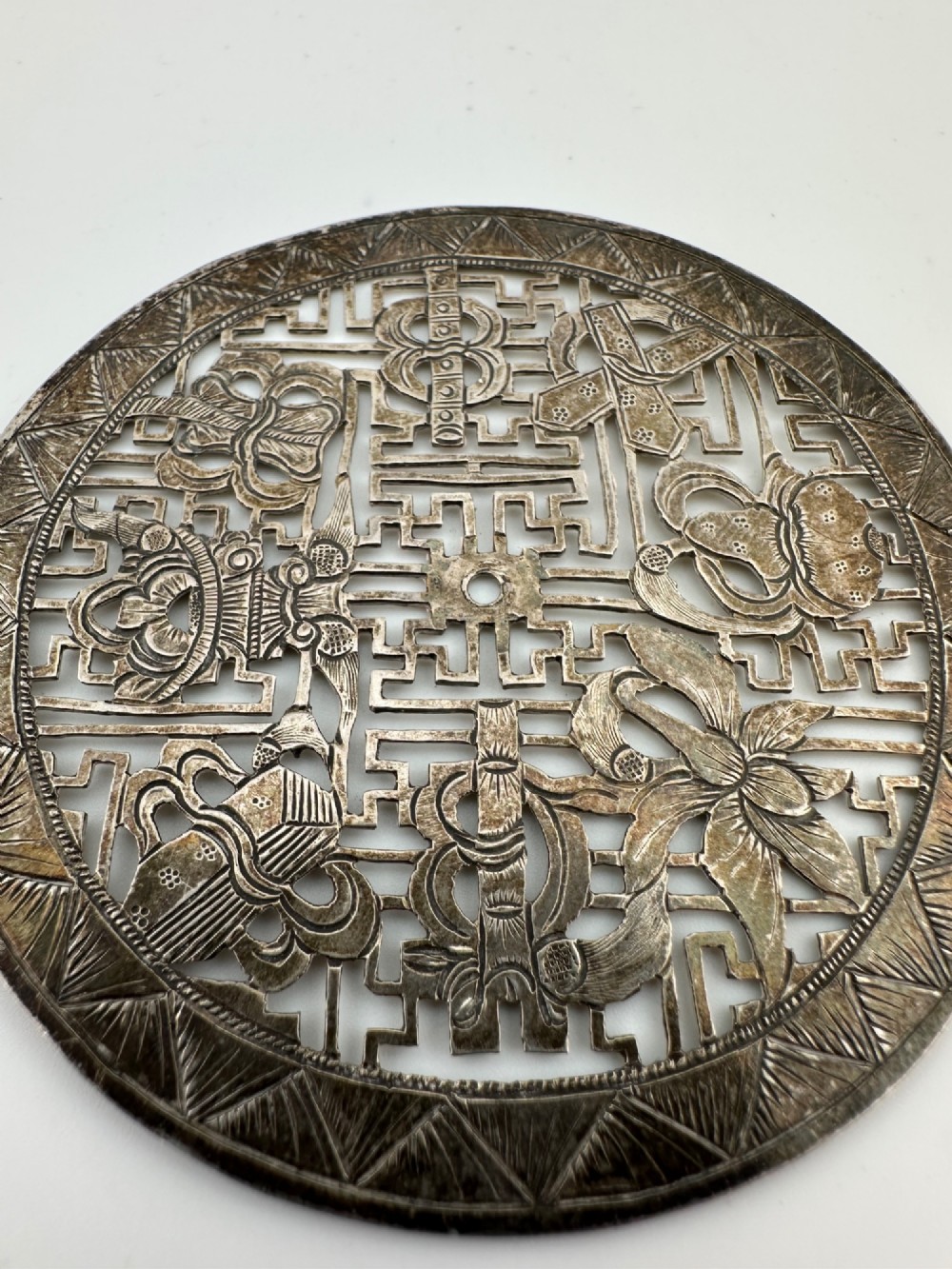A circular 19th-century Tibetan silver plaque featuring openwork fretwork and hand-engraved Buddhist auspicious symbols framed by a geometric border.