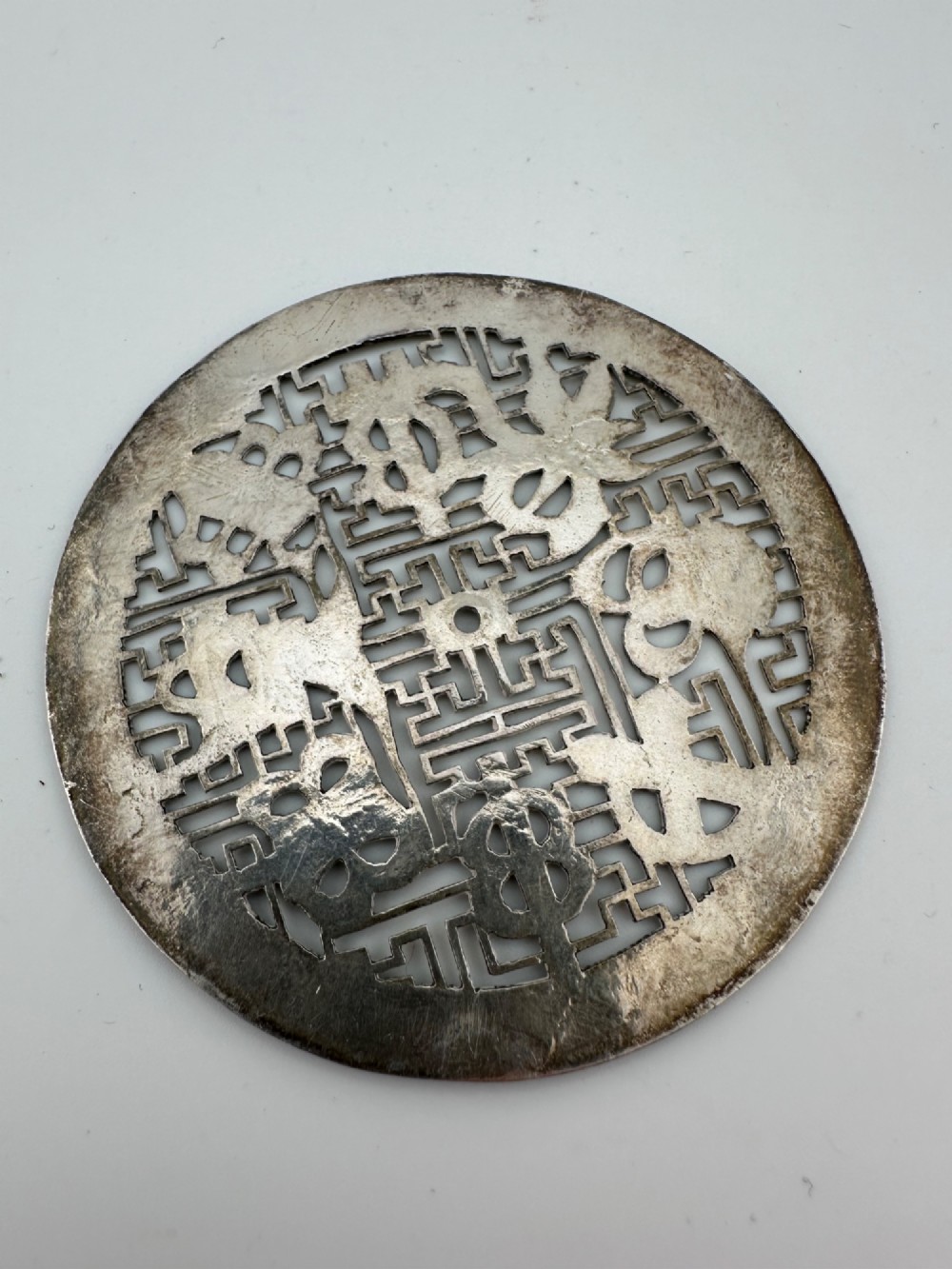 A circular 19th-century Tibetan silver plaque featuring openwork fretwork and hand-engraved Buddhist auspicious symbols framed by a geometric border. View II