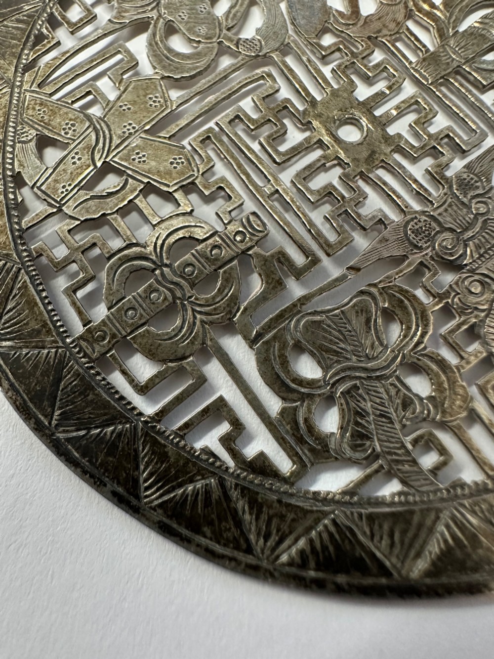A circular 19th-century Tibetan silver plaque featuring openwork fretwork and hand-engraved Buddhist auspicious symbols framed by a geometric border. View III