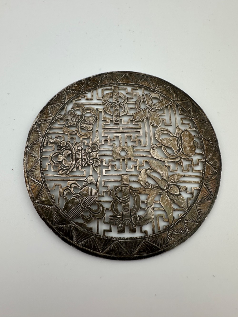 A circular 19th-century Tibetan silver plaque featuring openwork fretwork and hand-engraved Buddhist auspicious symbols framed by a geometric border. View IV