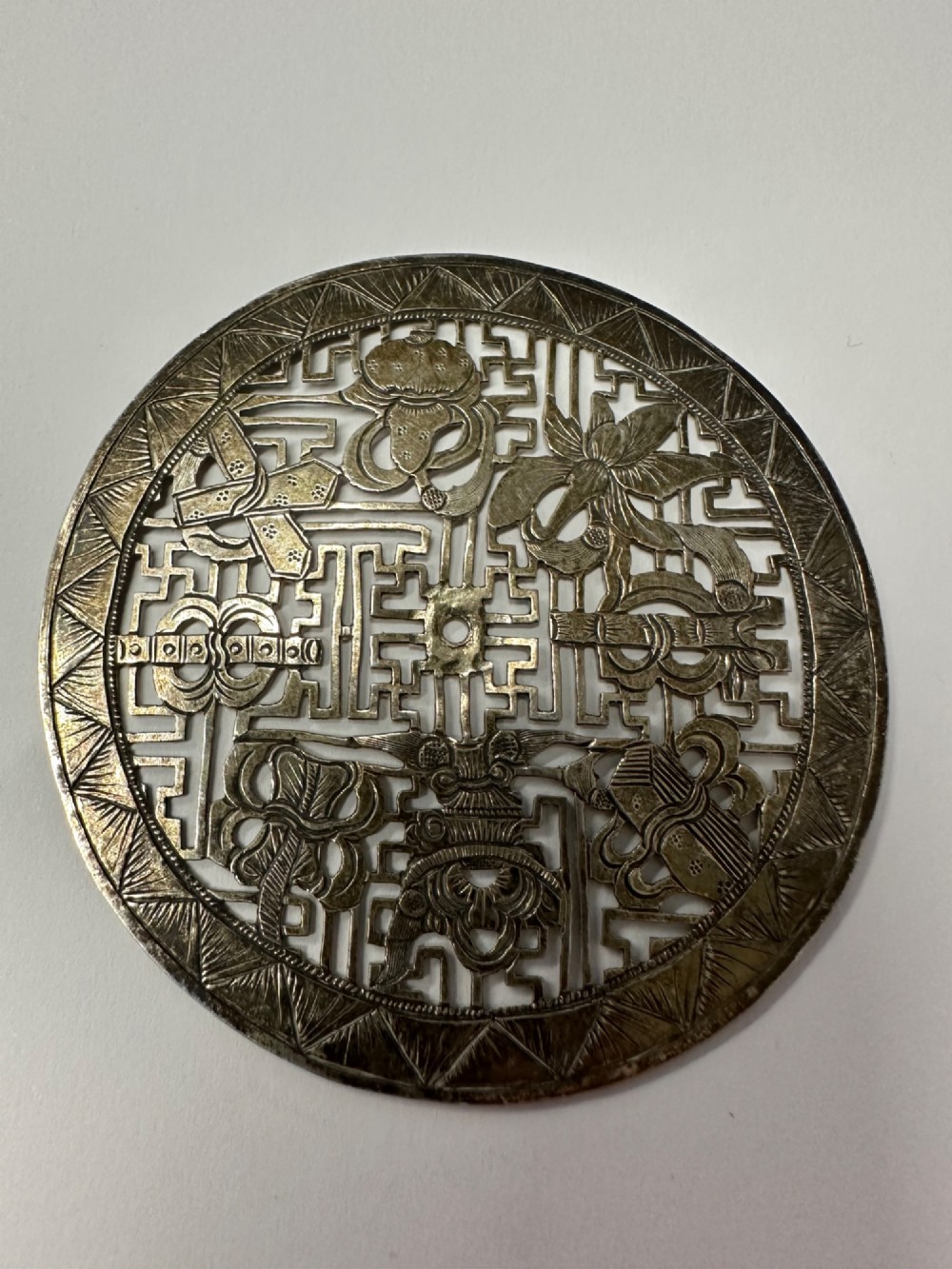A circular 19th-century Tibetan silver plaque featuring openwork fretwork and hand-engraved Buddhist auspicious symbols framed by a geometric border. View V