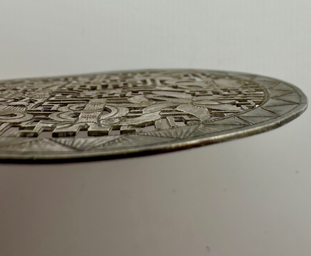 A circular 19th-century Tibetan silver plaque featuring openwork fretwork and hand-engraved Buddhist auspicious symbols framed by a geometric border. View VI