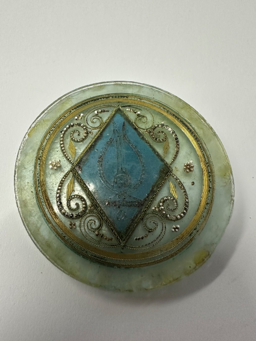 A circular glass Ottoman roundel featuring delicate gilt filigree scrollwork and a central diamond-shaped blue medallion with a calligraphic tughra.