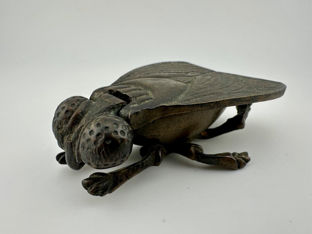 A cast dark brass match holder sculpted in the detailed shape of a fly with textured wings, compound eyes, and six legs.