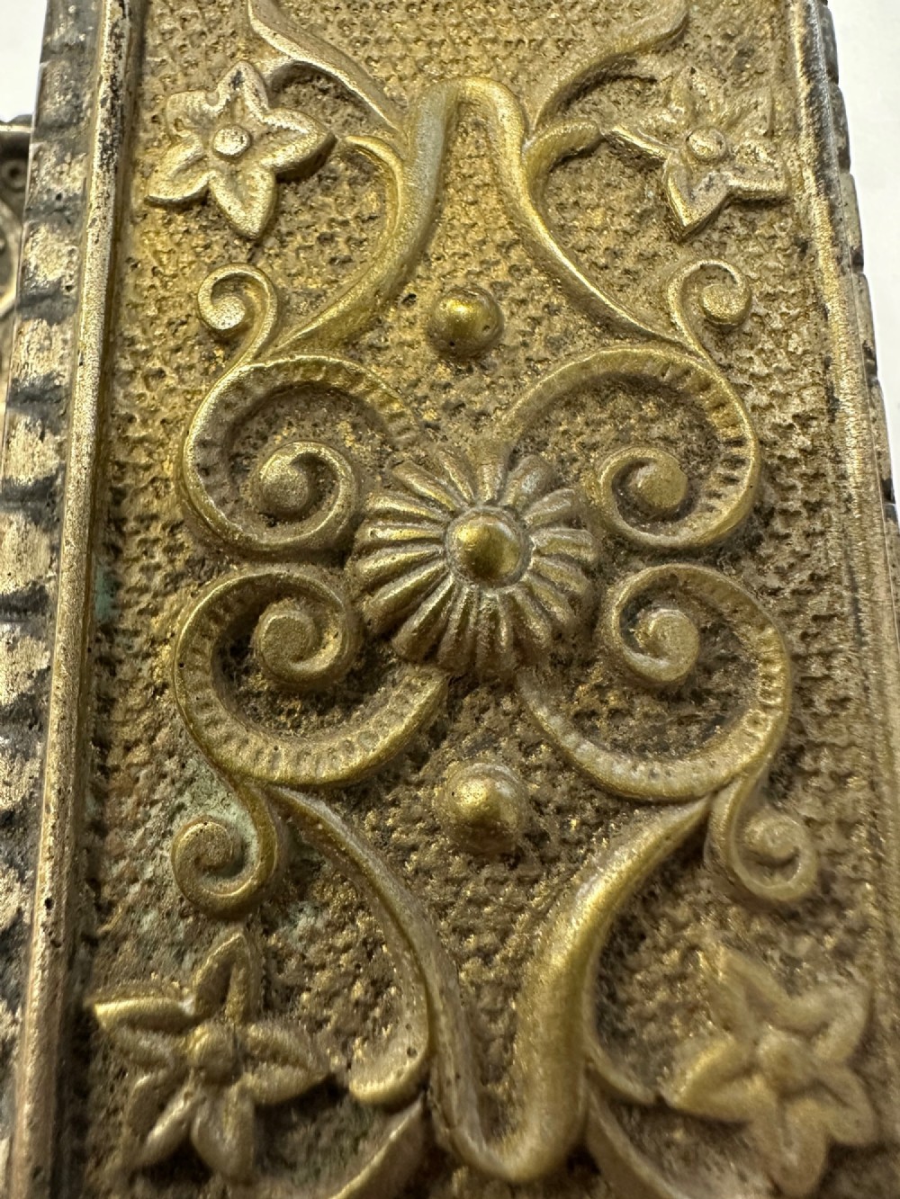 An antique silvered brass desktop vesta box with a hinged floral embossed lid, ribbed striker strip, and front tray resting on a beaded base. View X