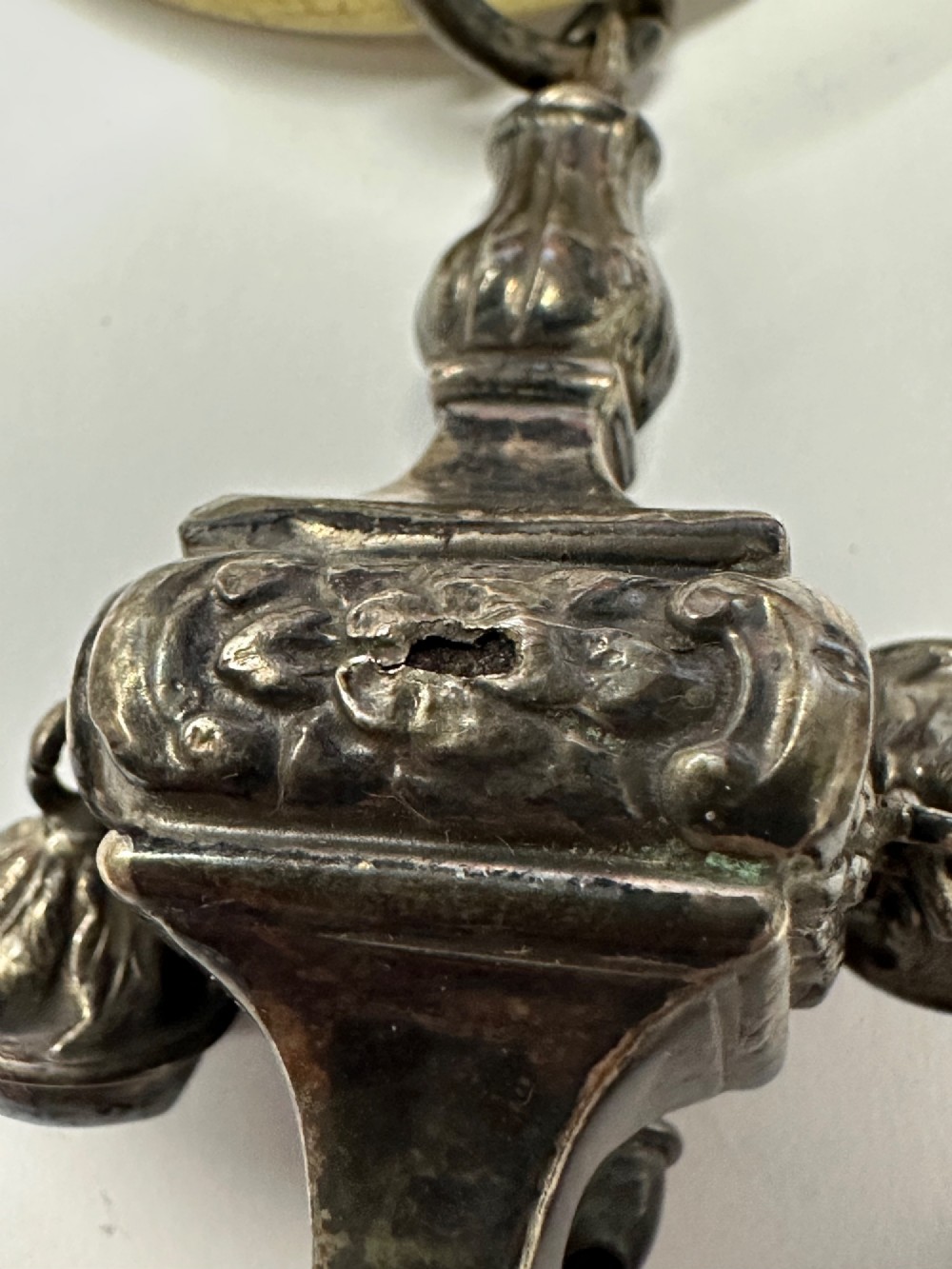 An antique silver baby rattle featuring embossed metalwork, small attached bells, and a cream-coloured circular teether ring. View IX