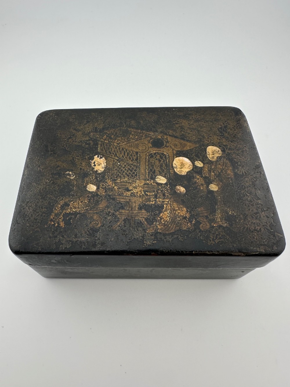 An early 19th-century rectangular black lacquer box with gilded painted Chinese figural scenes on the lid.
