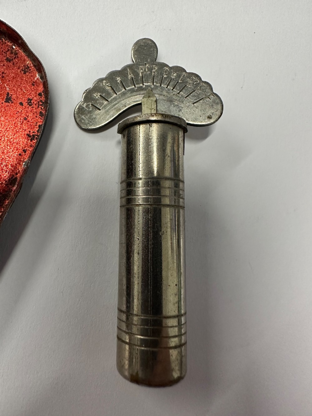 A cylindrical nickel-plated chromatic variable pitch pipe with a note scale arc sitting inside its open red metal case. View III
