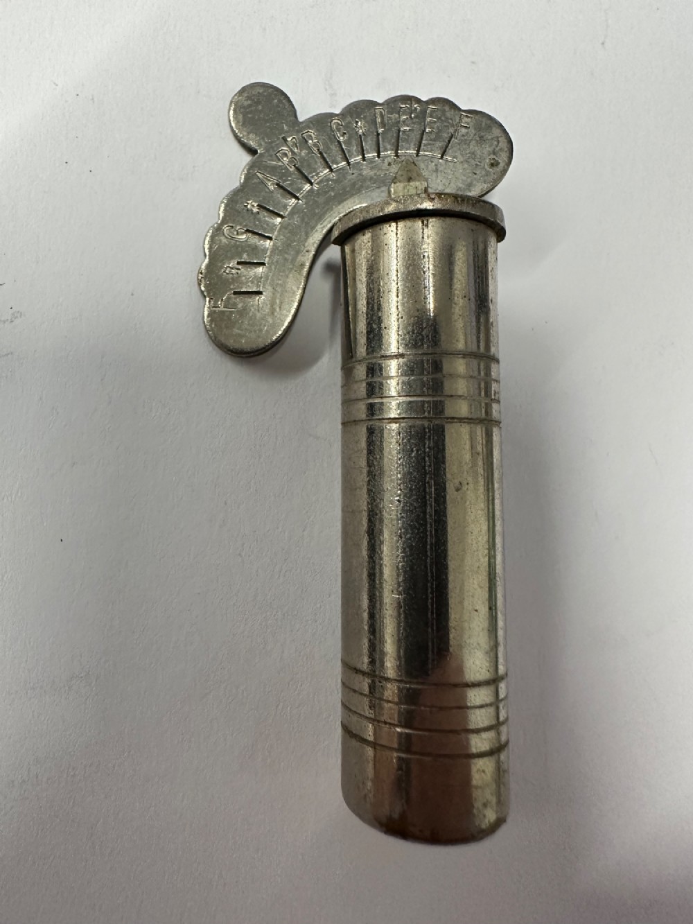 A cylindrical nickel-plated chromatic variable pitch pipe with a note scale arc sitting inside its open red metal case. View IX